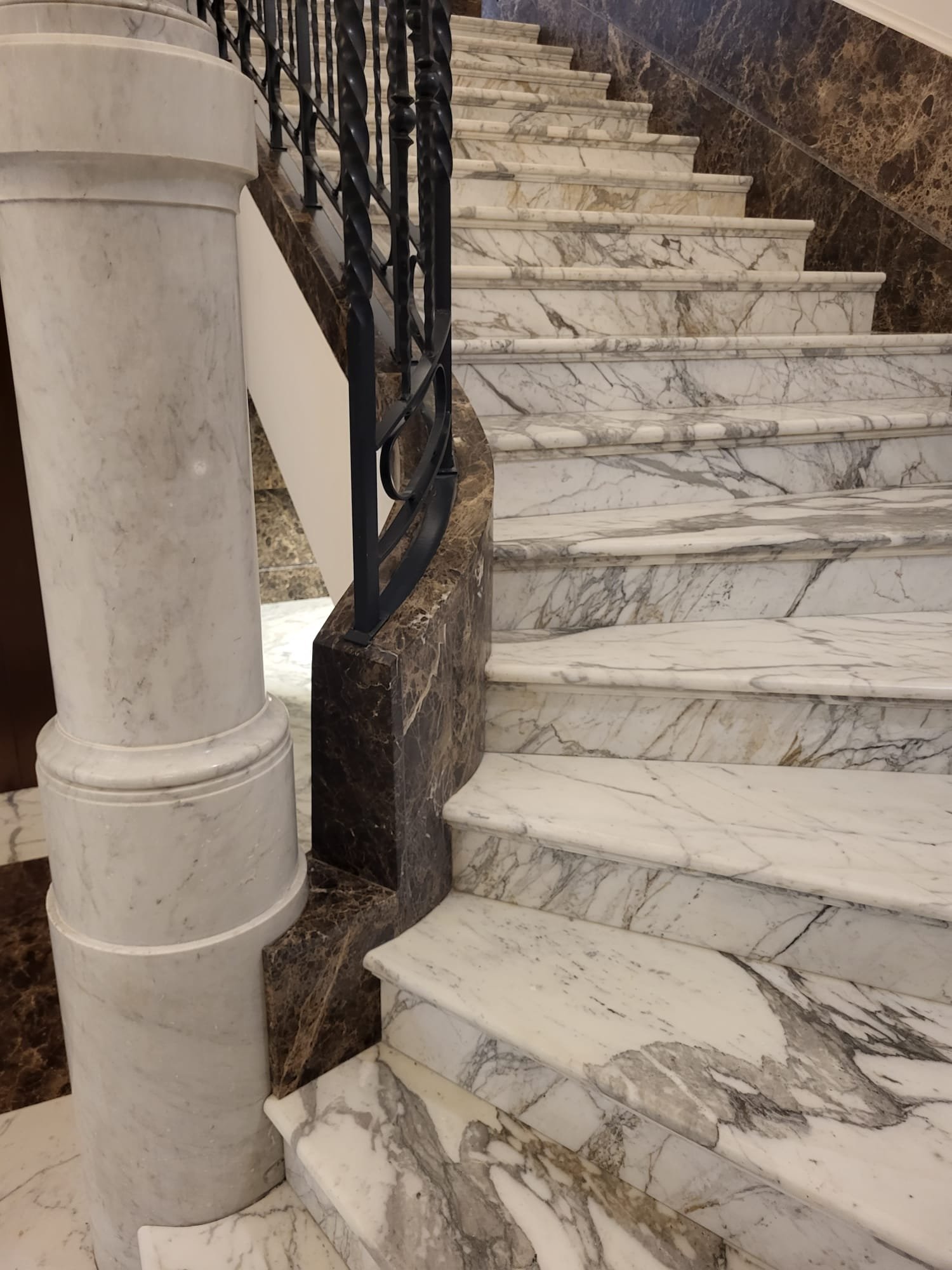 Scala in marmo venato con colonna in pietra e ringhiera in ferro